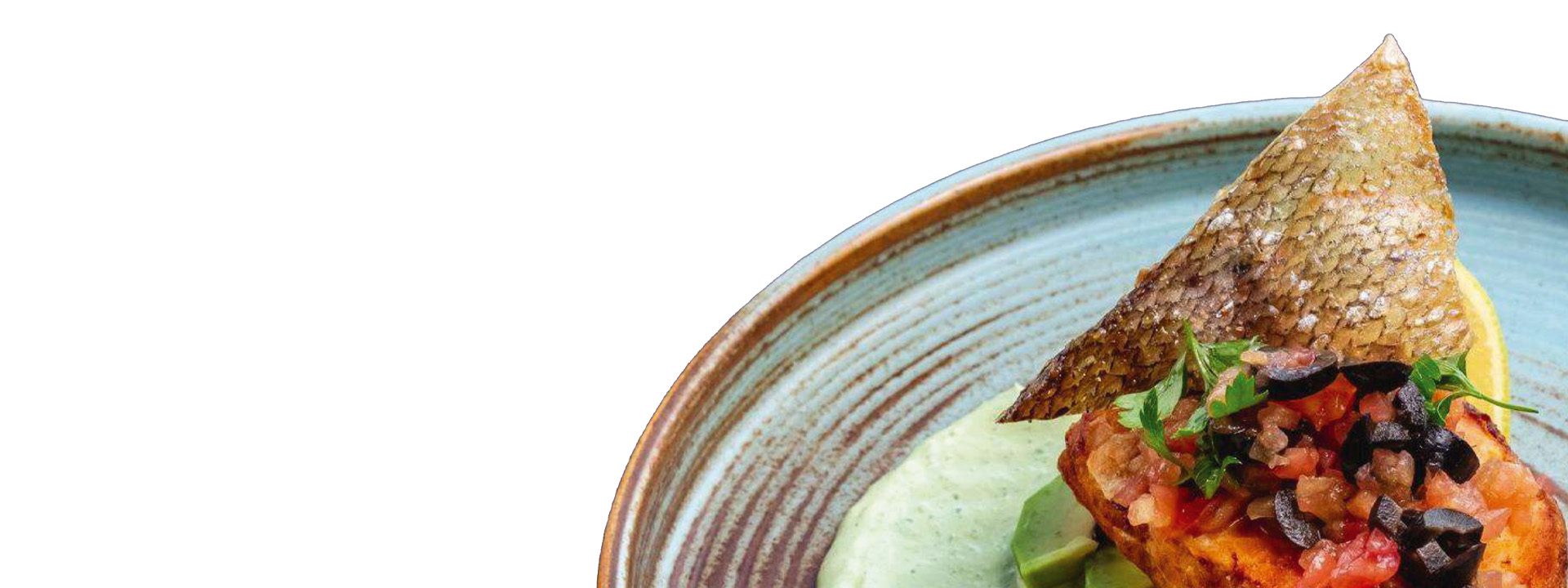 A plated dish featuring a piece of cooked fish with crispy skin, topped with diced tomatoes and olives, served on a green sauce.