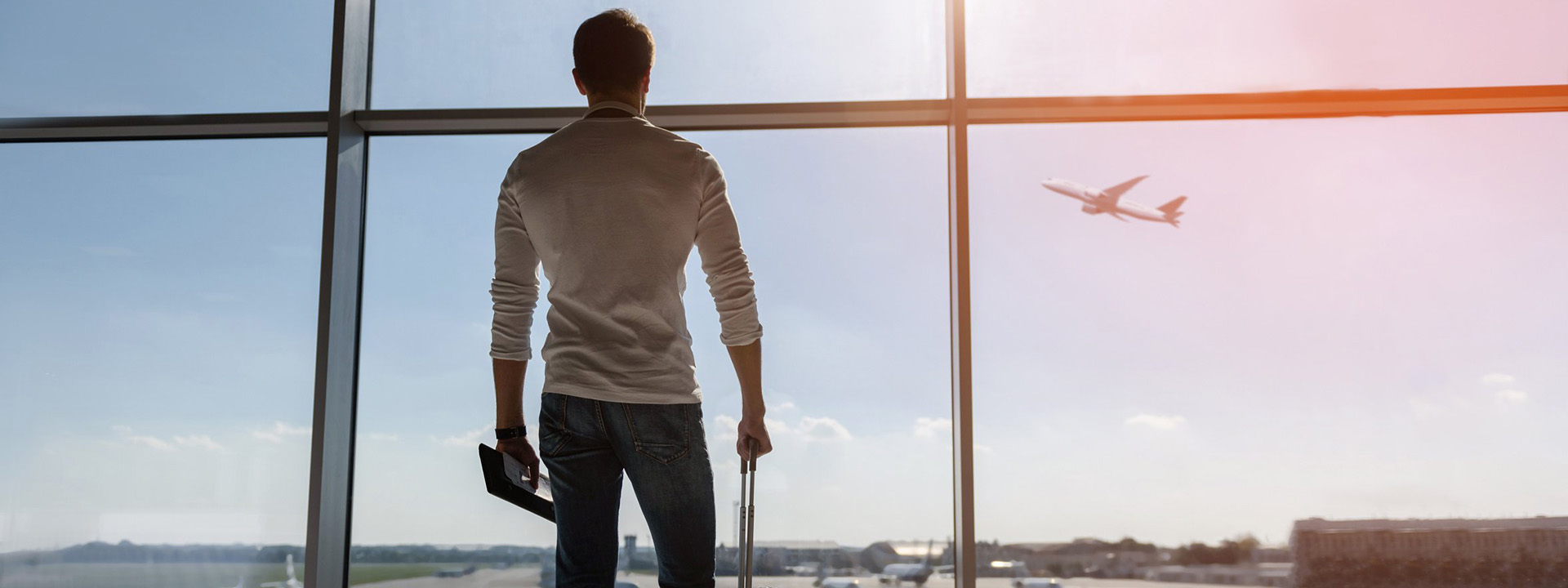 A person with a suitcase looking out a window at an airplane