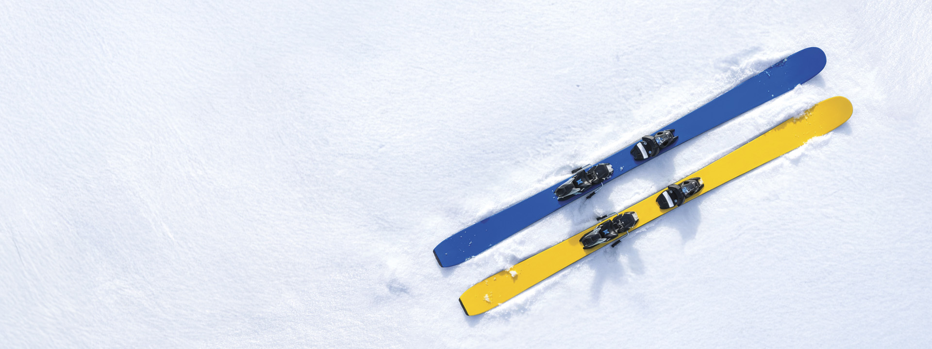 A pair of skis, one blue and one yellow, resting parallel on a snow-covered surface.