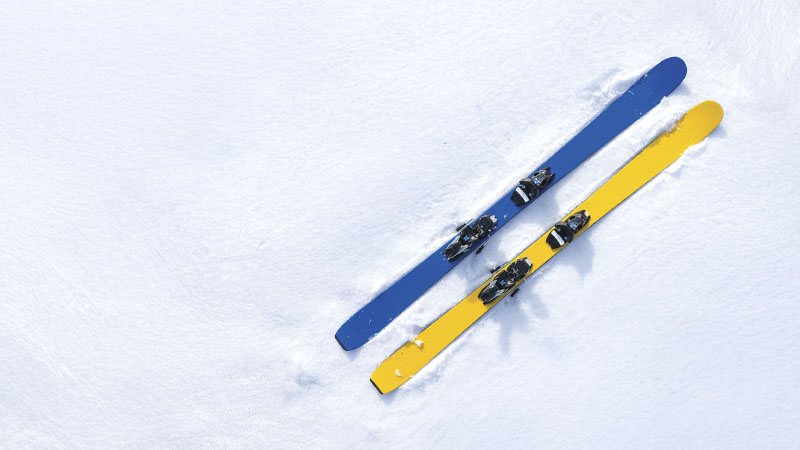 A pair of skis, one blue and one yellow, resting parallel on a snow-covered surface.