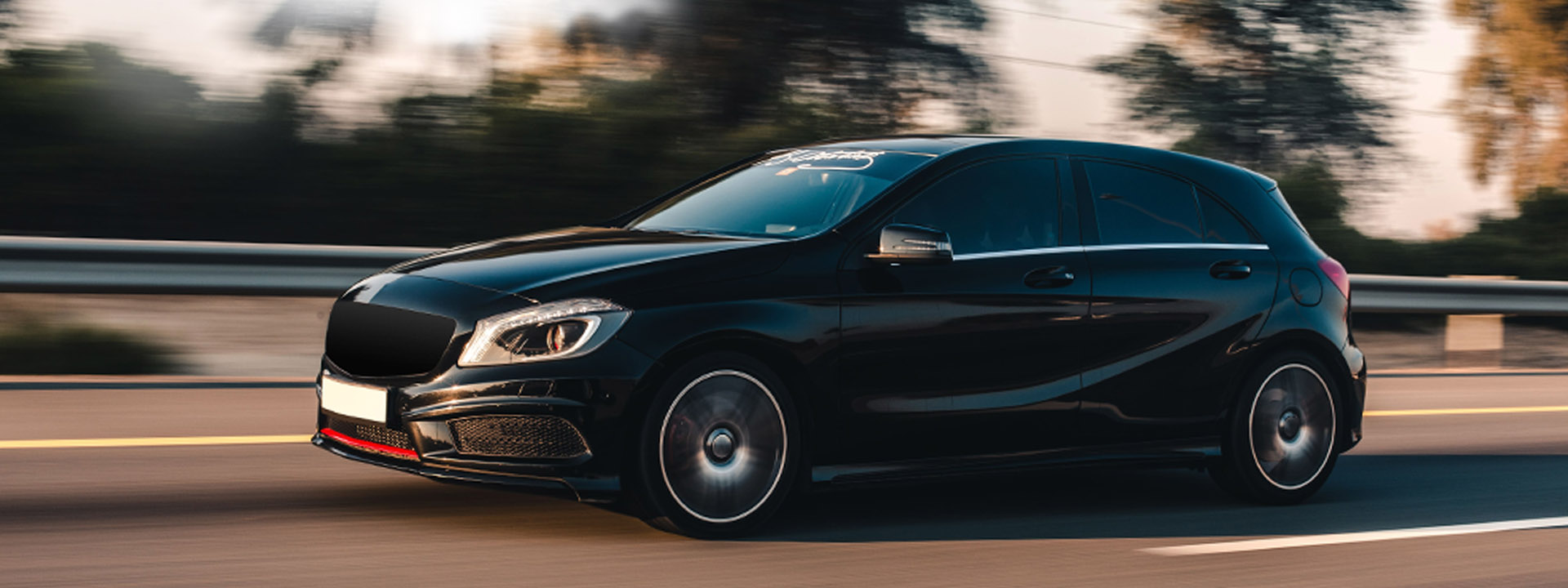 A black hatchback speeding on a highway with motion blur in the background.