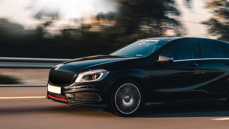 A black hatchback speeding on a highway with motion blur in the background.